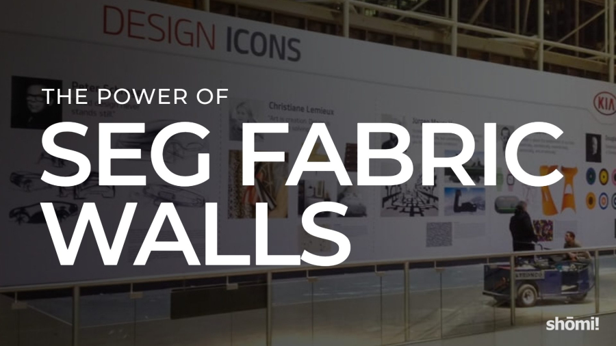 A large printed fabric wall display featuring the words The Power of SEG Fabric Walls in bold text stands out in a modern exhibition space, where people interact and explore the impressive fabric walls nearby.