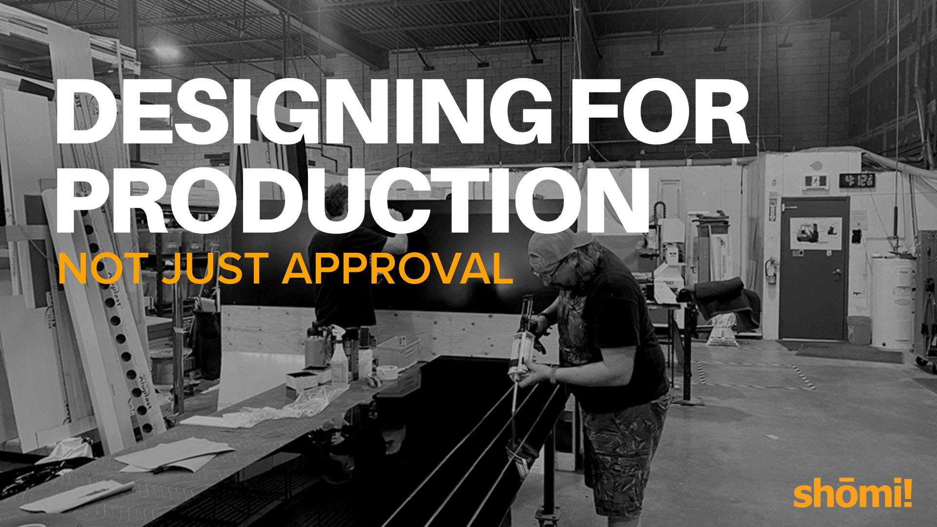 Black and white image of a man working in a factory or workshop with text overlaid: “Designing for production, not just approval.” Highlighting the importance of designing for production. The shömi logo appears in the bottom right corner.